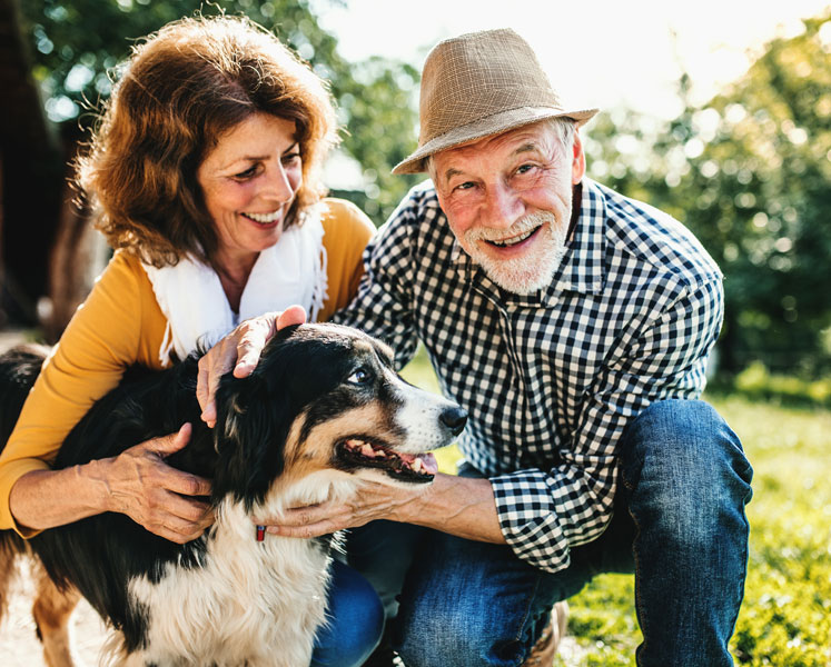 An older couple giving their dog affection outside on a sunny cool day.